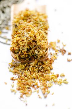 Vibrant dried yellow flower petals overflowing from a wooden scoop against a clean white background.