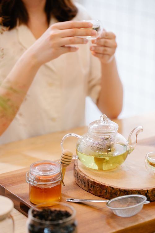 Free Elegant tea setup featuring a glass teapot, honey jar, and hands holding a cup. Perfect for lifestyle themes. Stock Photo