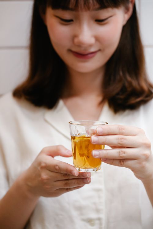 Free A young woman smiling and holding a glass of tea. Warm and inviting indoor scene. Stock Photo