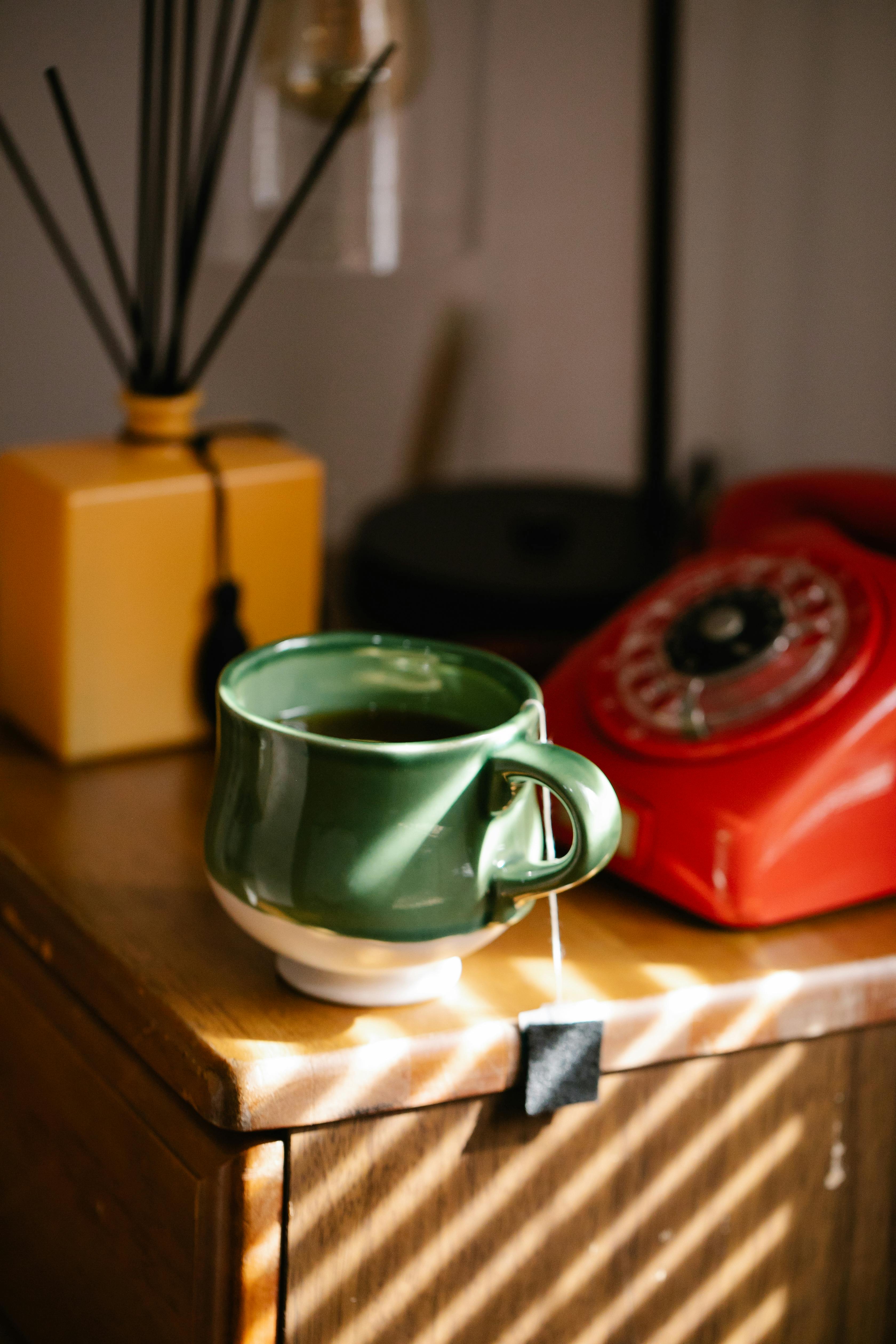 Free Warm and inviting interior scene featuring a green tea cup and vintage rotary phone on a wooden dresser. Stock Photo