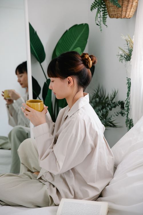 Free A serene scene of a woman sipping coffee indoors, surrounded by greenery and cozy decor. Stock Photo