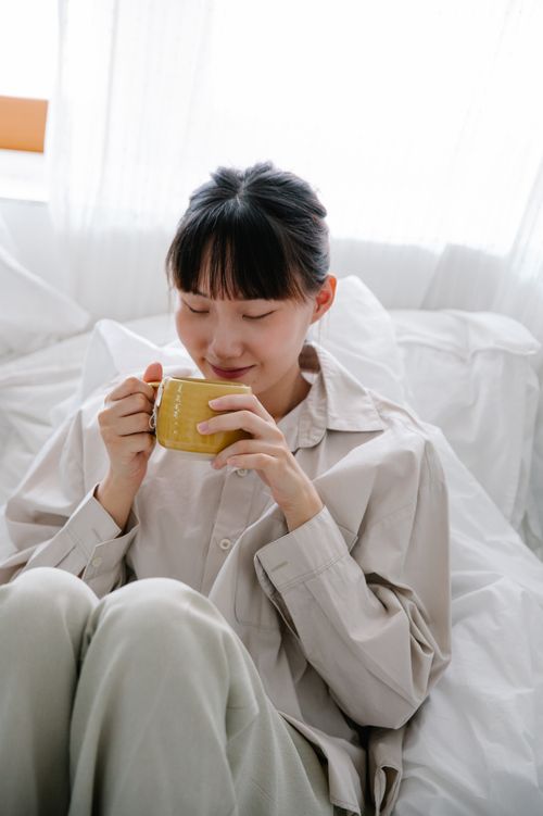 Free Woman sitting in bed, savoring a warm drink with a peaceful smile. Stock Photo