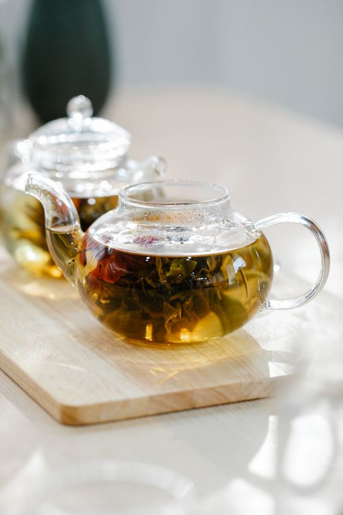 Free A clear glass teapot filled with herbal tea is placed on a light wooden surface, capturing a warm ambiance. Stock Photo