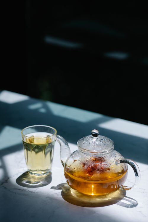 Free A clear glass teapot and cup with herbal tea, beautifully lit by natural sunlight. Stock Photo