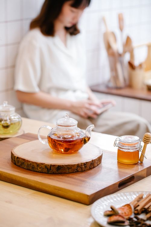 Free Glass teapot with tea and honey jar on table in a cozy room setting. Stock Photo