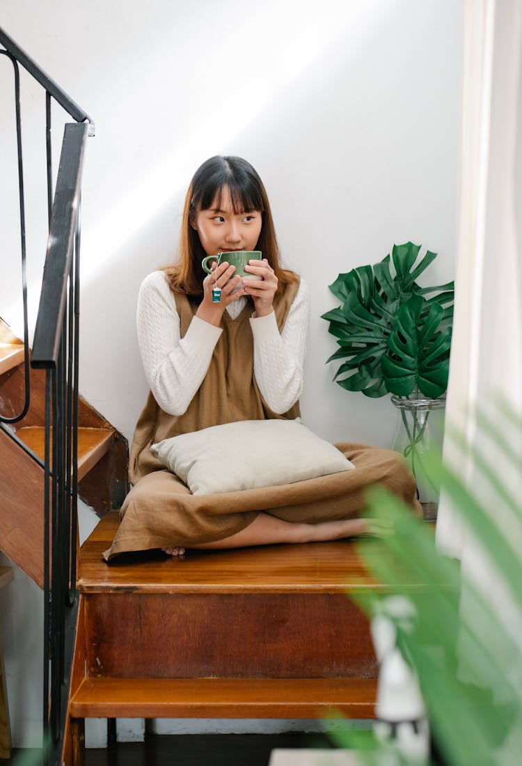 Young Woman Sitting On Stairs Drinking Tea