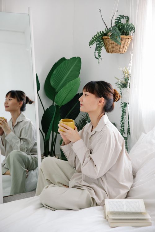 Free Peaceful morning scene of a woman in pajamas enjoying coffee by a mirror with houseplants. Stock Photo