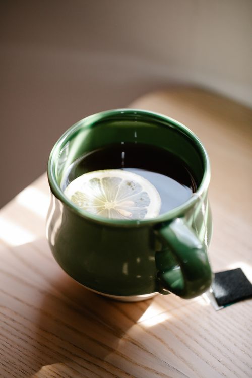 Free A green ceramic mug with black tea and a lemon slice on a wooden table. Stock Photo