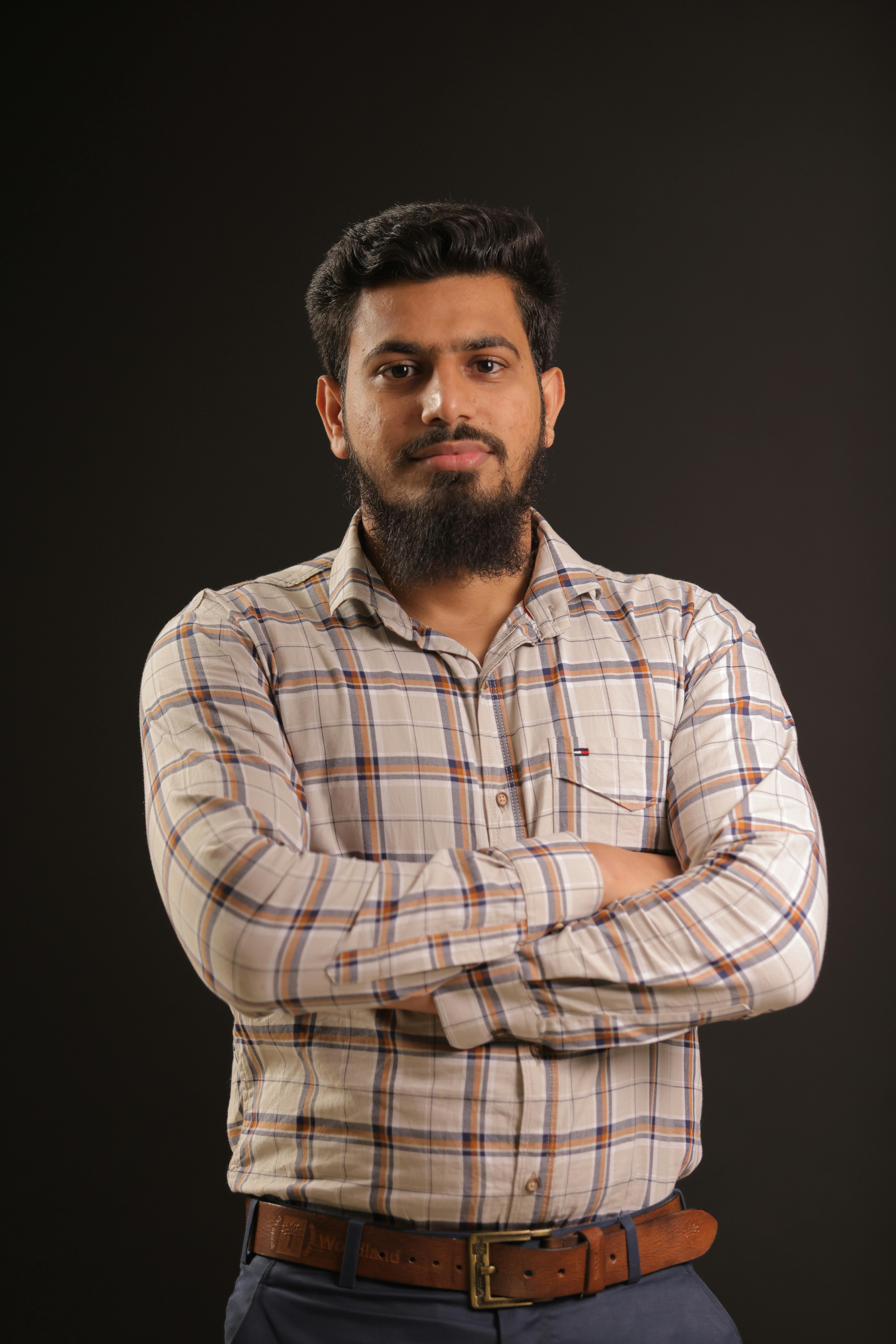 Portrait of a confident man with crossed arms against a black background in a studio setting.