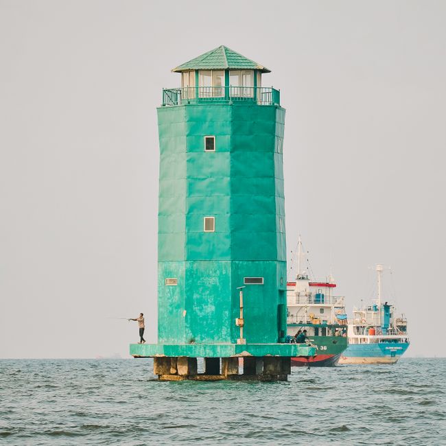 A striking green lighthouse stands tall on the sea with a ship in the background, evoking nautical themes.