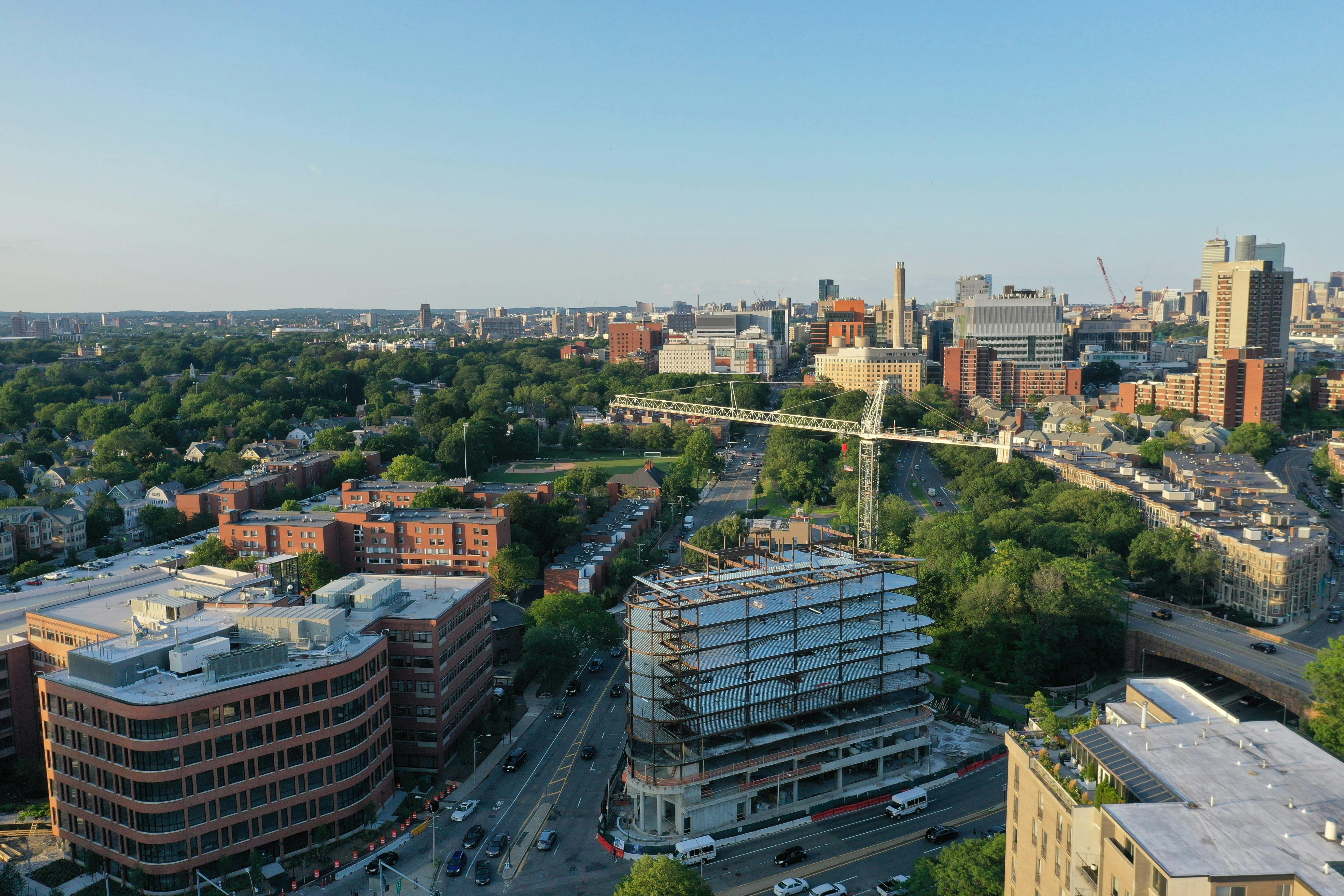 Aerial view of city with construction site and greenery, blue sky overhead.