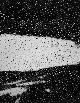 Close-up of raindrops on a glass window with a scenic background in grayscale.