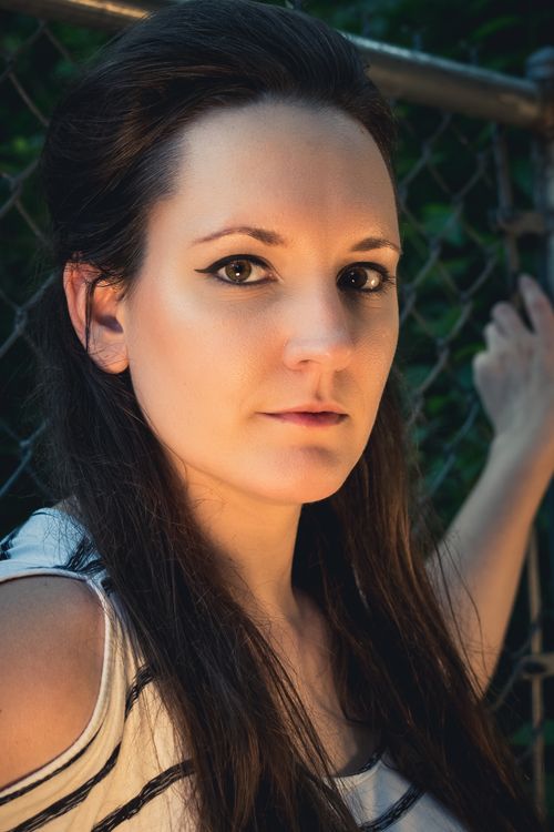 Free Close-up portrait of a woman standing outdoors by a chain-link fence. Stock Photo