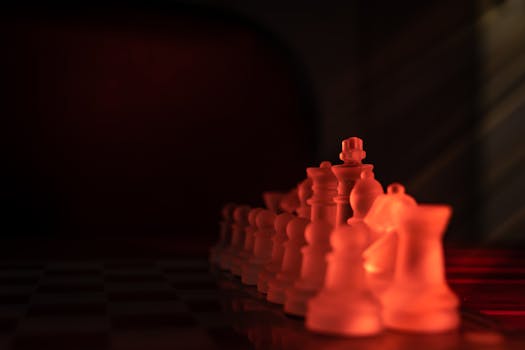 Close-up of chess pieces on a board under red lighting creating a dramatic effect.