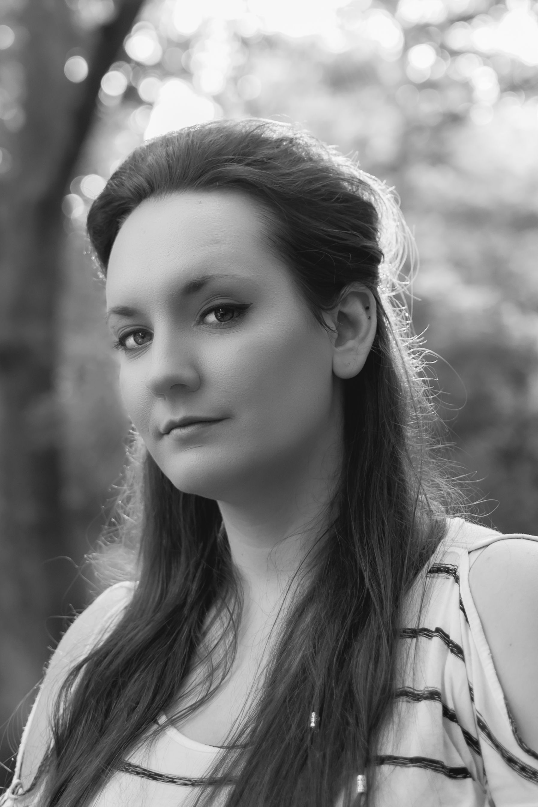 Artistic black and white portrait of a woman with long hair in an outdoor setting.