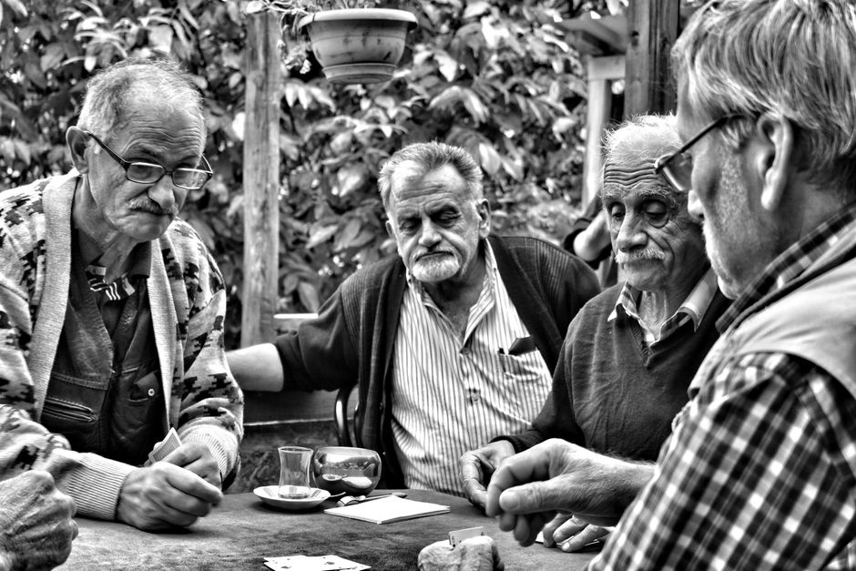 Cuatro hombres mayores disfrutan de un juego de cartas al aire libre en un café turco, capturado en blanco y negro.