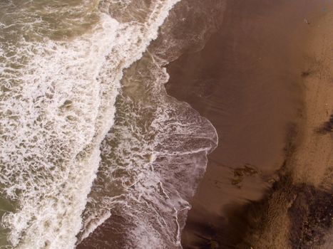A stunning aerial perspective of waves crashing on a serene sandy beach with beautiful sea patterns.
