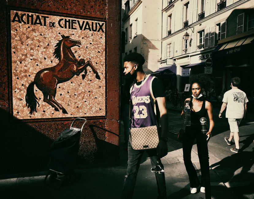 Street scene in Paris showing people with face masks, a mosaic, and Parisian architecture.