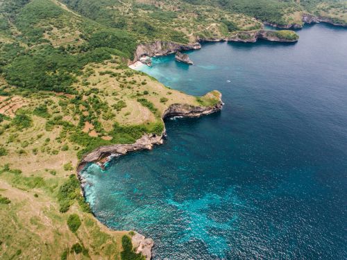 Free A breathtaking aerial view of a rugged coastline with vibrant blue water and lush green cliffs. Stock Photo