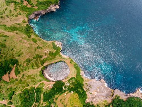 Free Breathtaking aerial view of a coastal lagoon with natural rock formations meeting the vibrant blue ocean. Stock Photo
