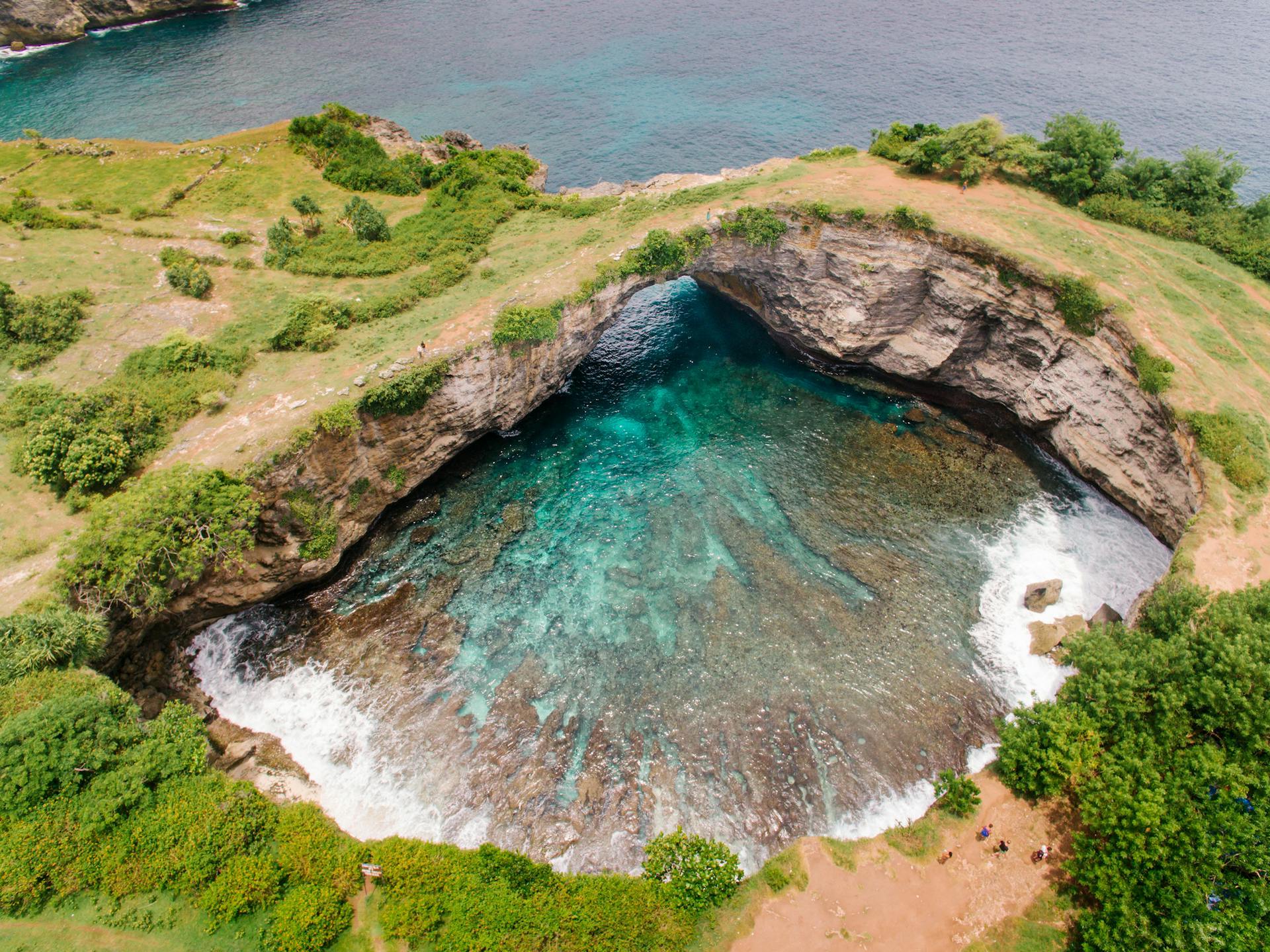 Breathtaking aerial view of a coastal sinkhole with stunning blue lagoon waters, surrounded by lush greenery.