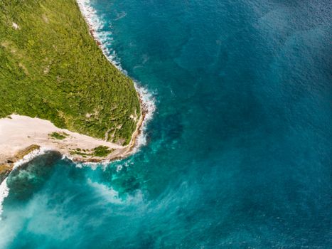 Stunning aerial view of a turquoise ocean coastline with vibrant waves and lush greenery.
