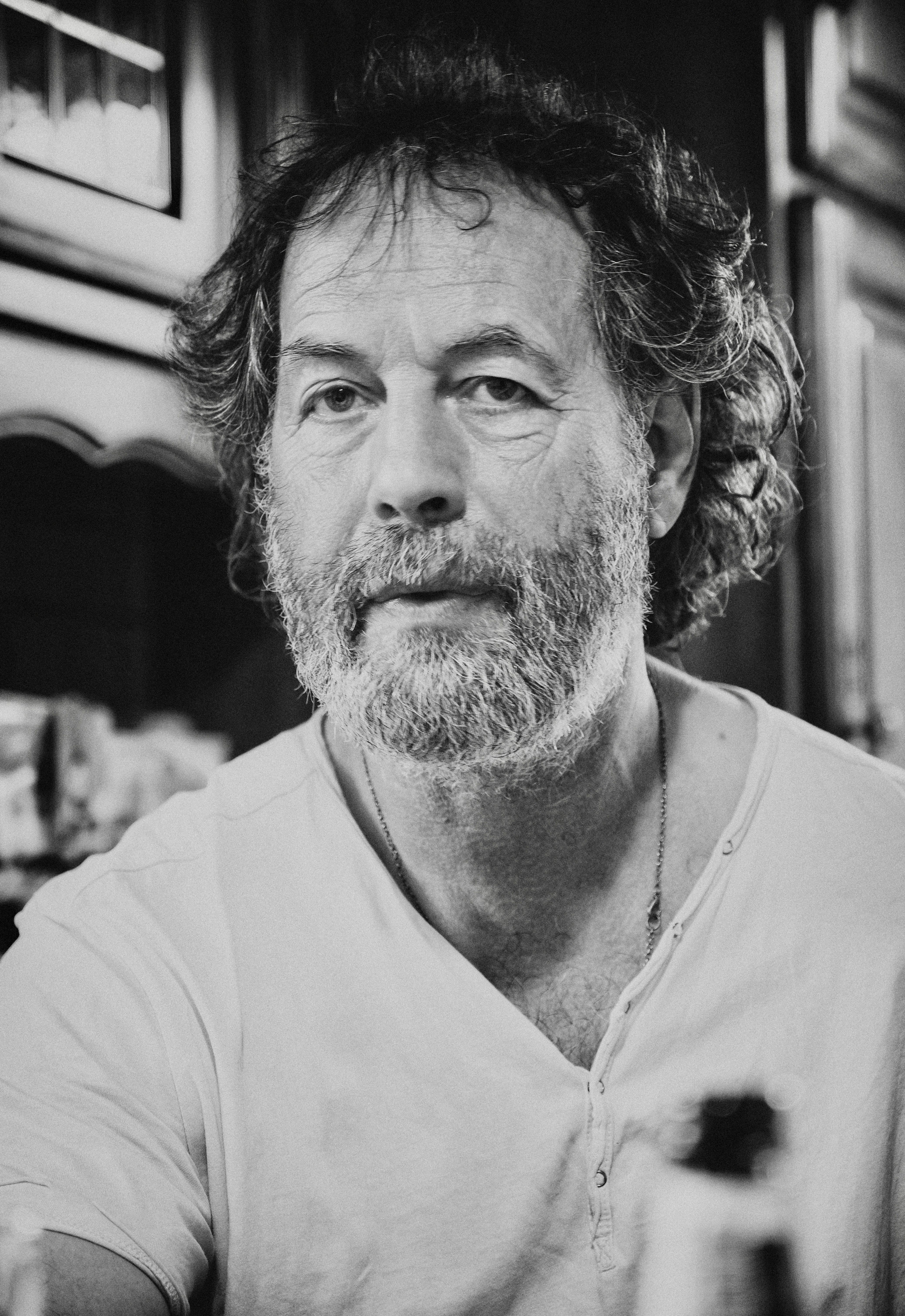 Moody black and white portrait of a bearded adult man indoors, conveying seriousness.