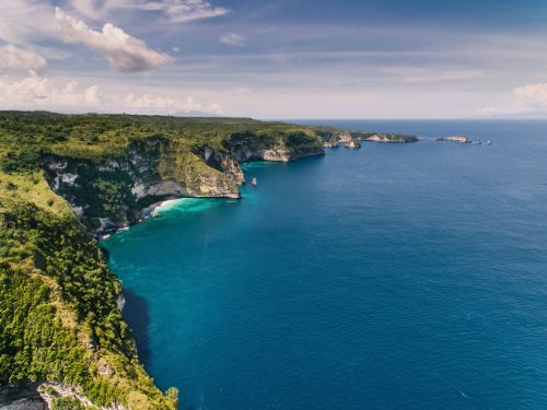 Free A breathtaking aerial view showcasing a lush green cliffside meeting the deep blue ocean under a partly cloudy sky. Stock Photo
