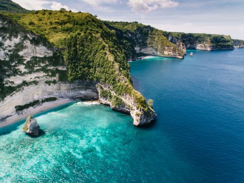 Free Stunning aerial shot of cliffs with lush greenery and turquoise ocean waters. Stock Photo