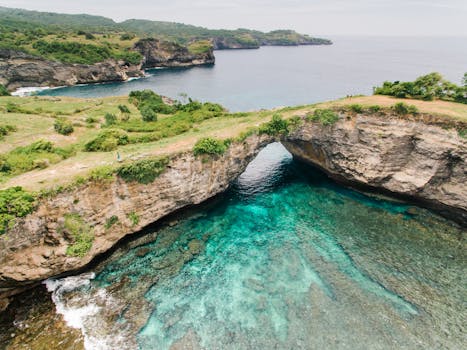 A stunning aerial shot capturing a natural rock arch over turquoise waters with lush green surroundings.