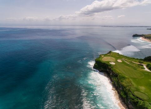 A breathtaking aerial view of a coastal golf course along a rocky shoreline with turquoise ocean waves.