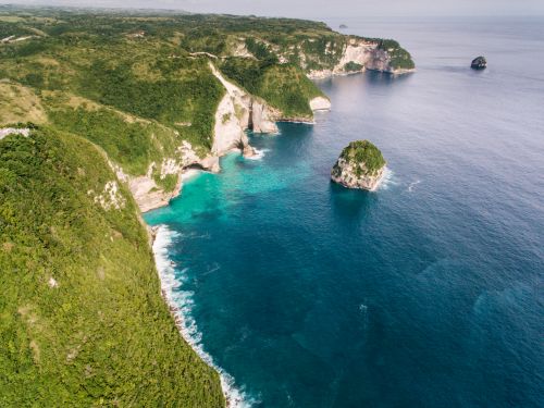 Free Dramatic aerial view of rugged coastal cliffs and turquoise sea waves crashing against them. Stock Photo