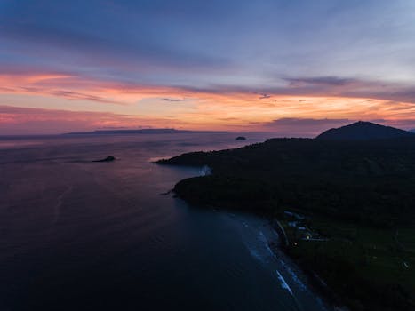 A captivating aerial view of a sunset over the ocean and island with vibrant colors.