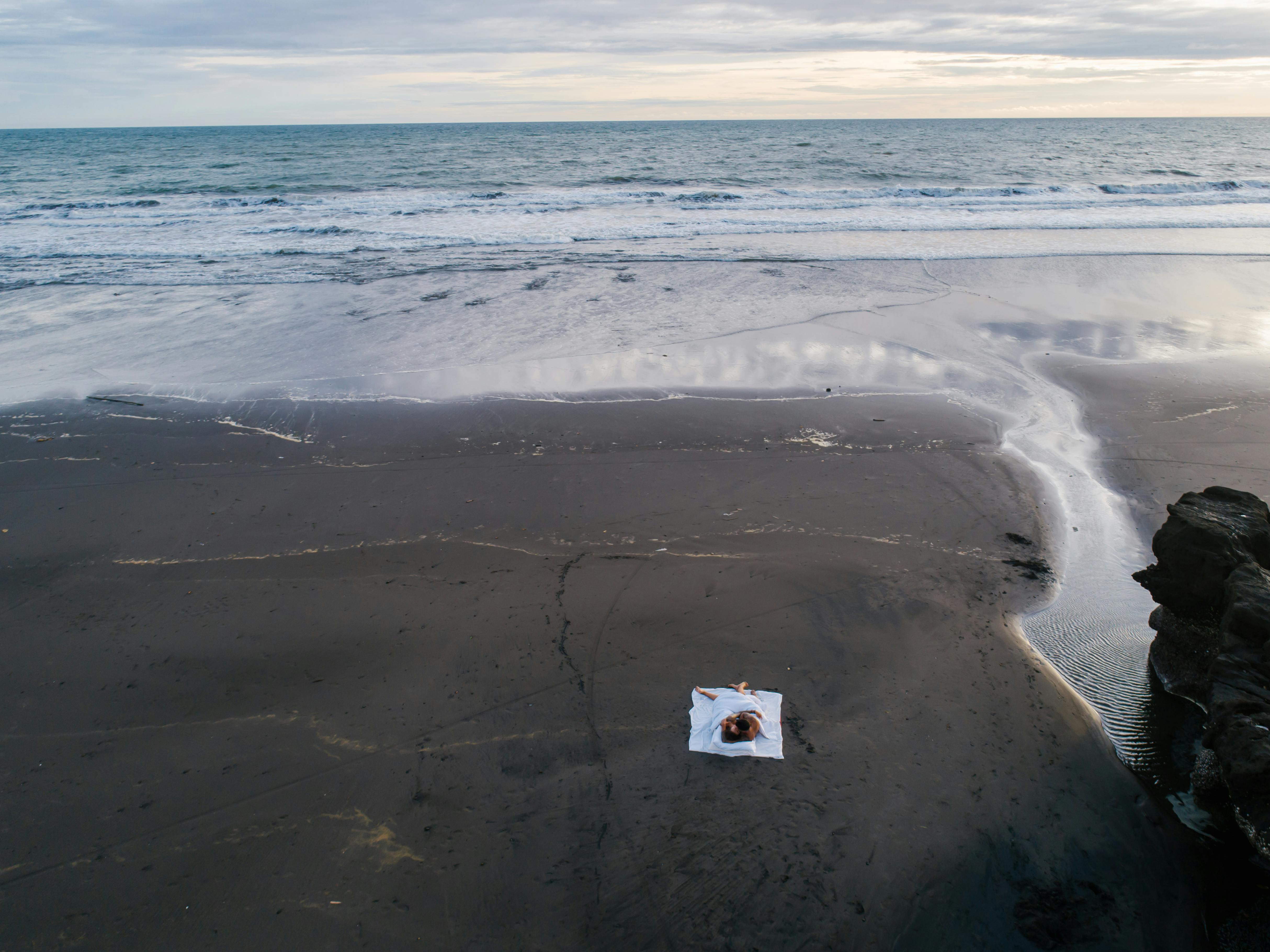 Aerial view of a couple lying on a blanket at a secluded beach, embracing romance and tranquility.