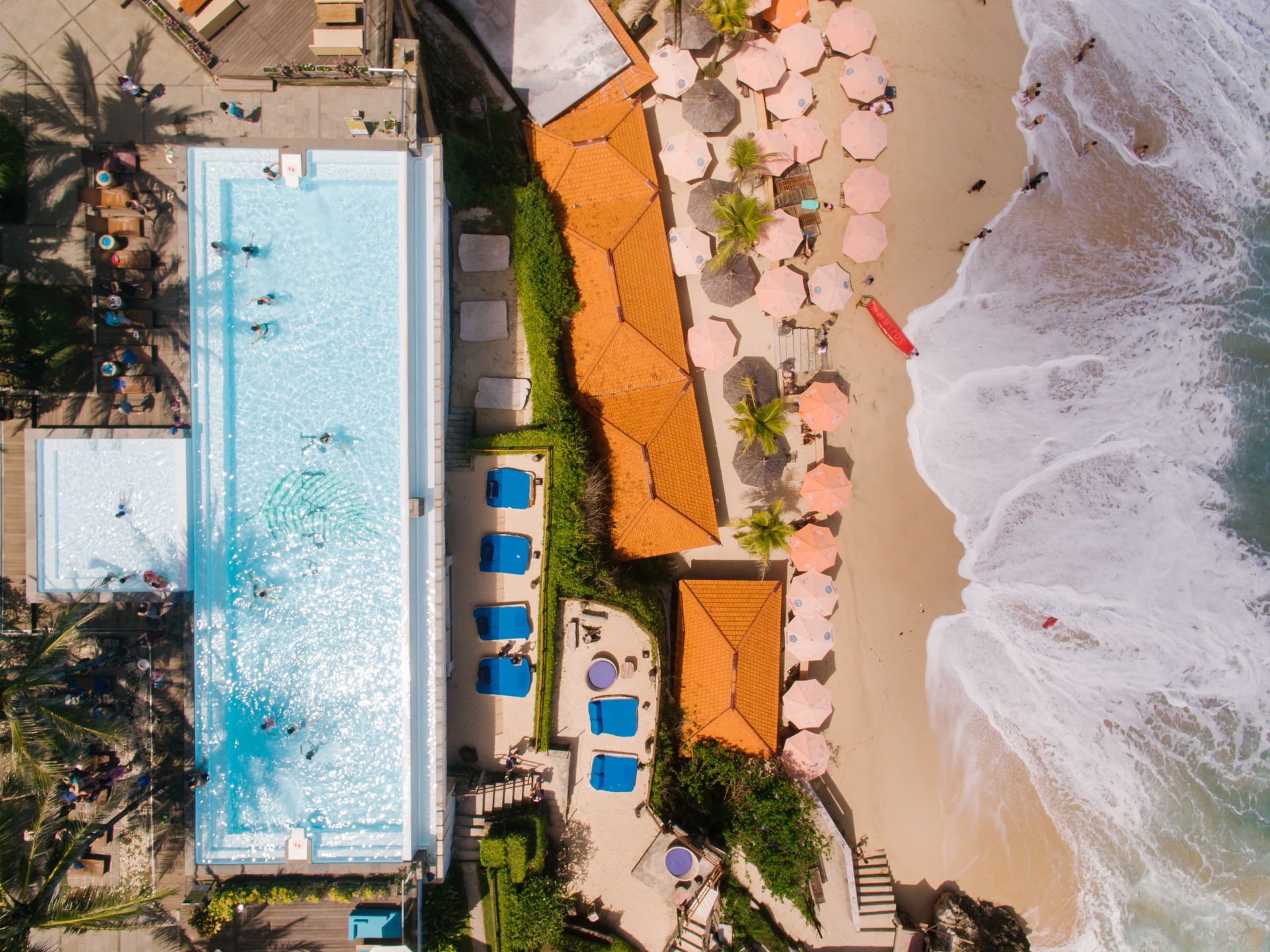 Stunning aerial view of a luxury beach resort with pool, sea, and sun loungers.