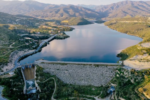 Breathtaking aerial view of a dam and reservoir nestled in lush green hills, showcasing a serene landscape.