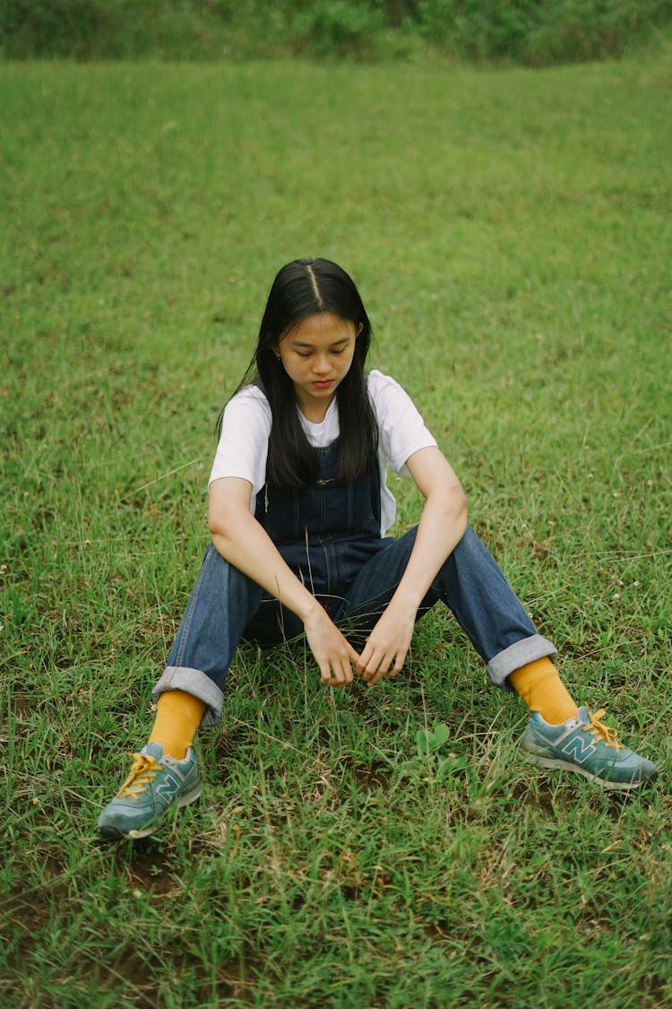 A Woman In Overalls Sitting On The Grass 