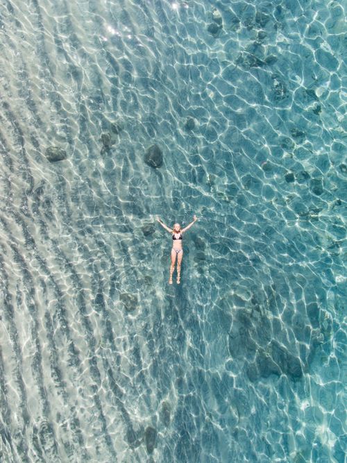 Free Aerial drone shot of a woman leisurely floating in a crystal clear blue sea, showcasing serenity and relaxation. Stock Photo