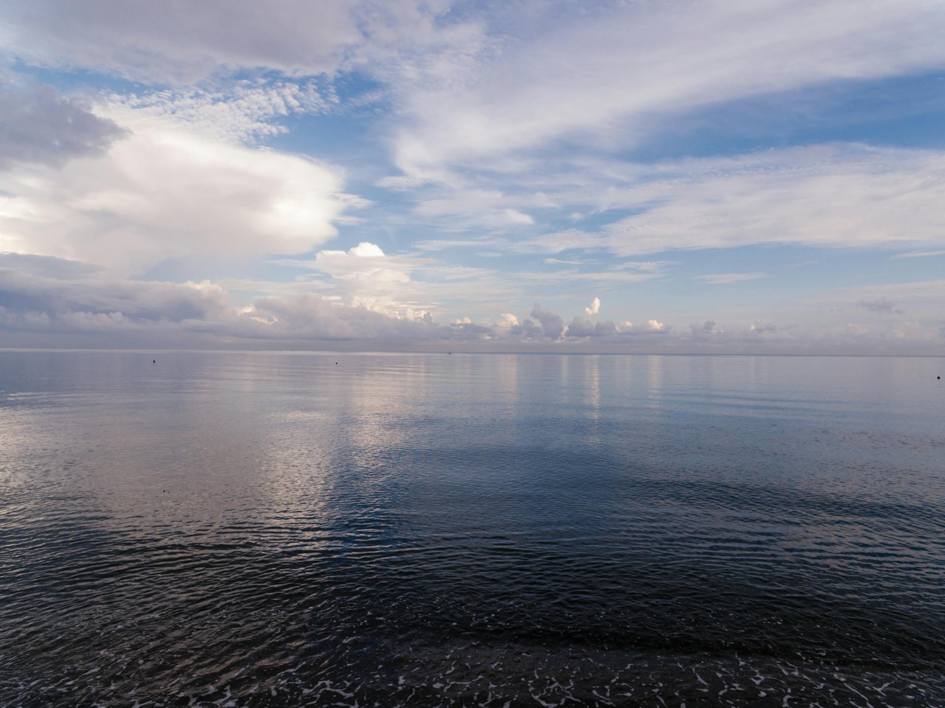 Peaceful ocean landscape with calm water and dramatic clouds under a blue sky.