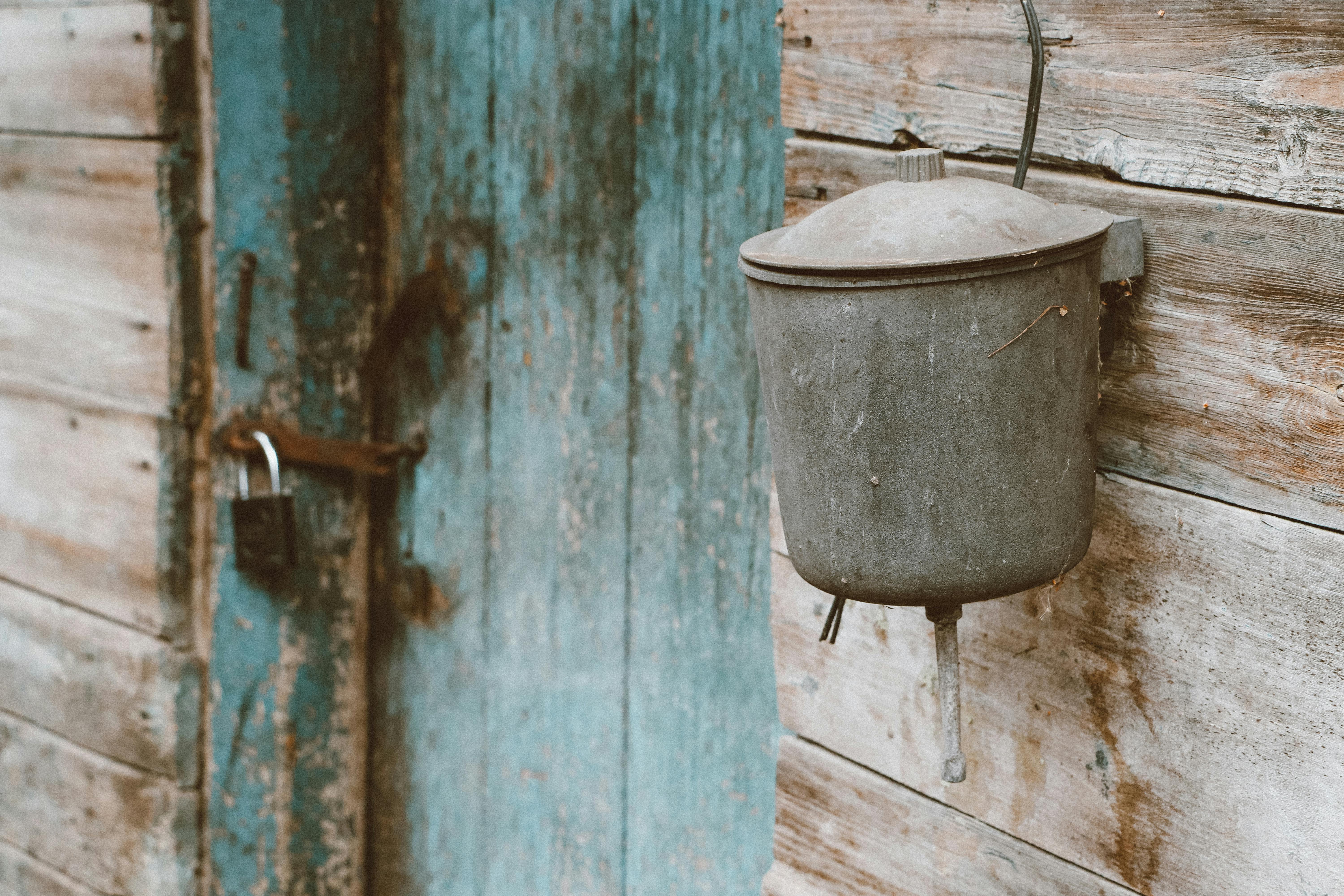 Close-up of a rustic wooden wall with a vintage bucket and padlocked blue door, evoking an aged, secure look.