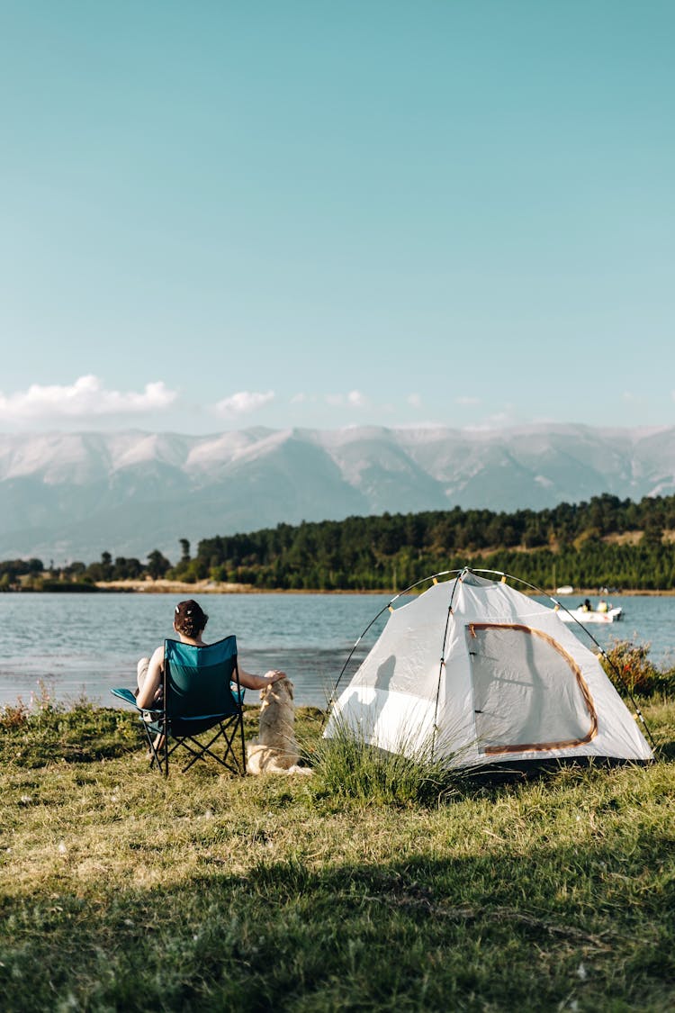 A Person Sitting On A Folding Chair And A Dog Near A Tent