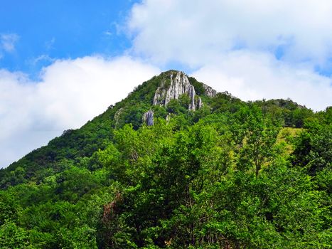 蔚蓝的天空下，郁郁葱葱的绿色山峰上飘着蓬松的云层