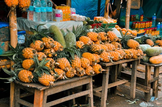 Fresh pineapples and other fruits displayed at a bustling outdoor market, offering a tropical vibe.