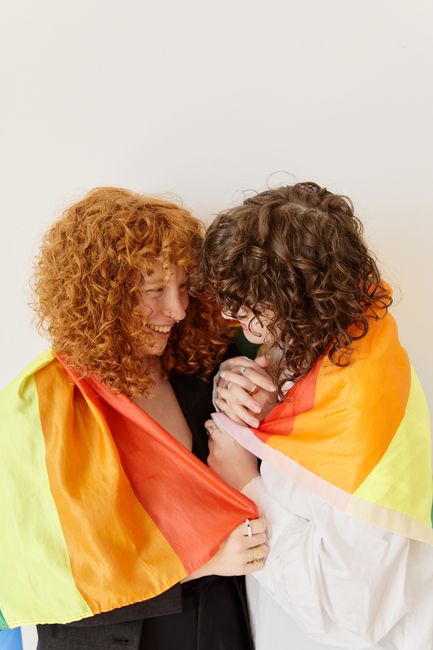 Joyful LGBTQ couple wrapped in a rainbow flag, celebrating love and diversity with smiles.