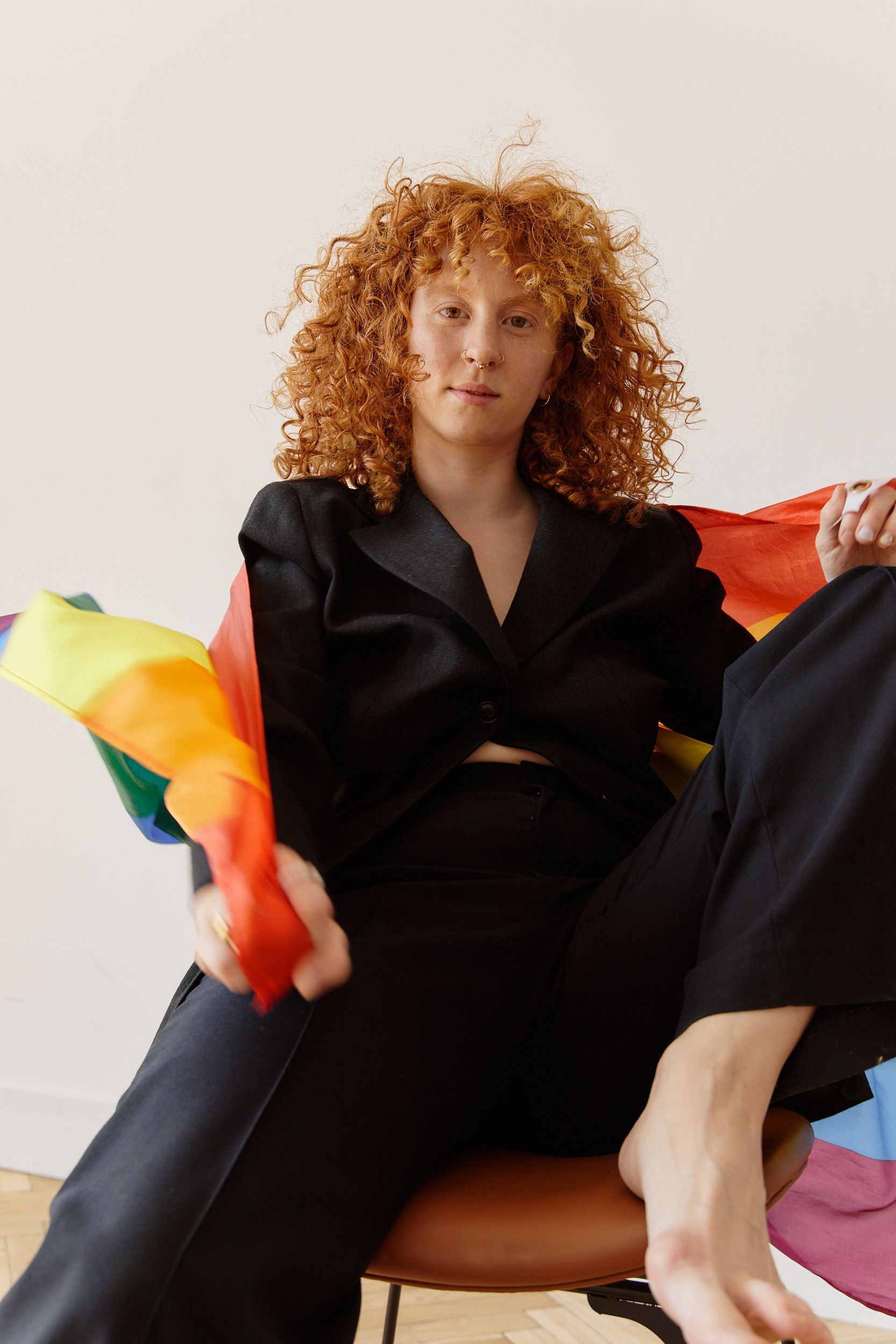 Young woman in a black suit with rainbow flag, confident pose indoors.