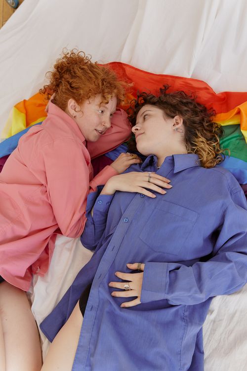 Free Two women embracing on a rainbow flag, symbolizing LGBTQ love and togetherness indoors. Stock Photo