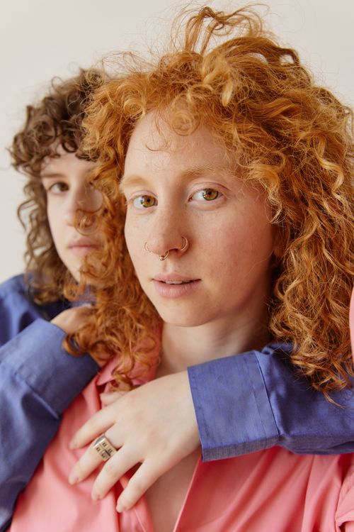 Free Close-up portrait of two women with curly hair, nose rings, embracing in a warm, intimate setting. Stock Photo