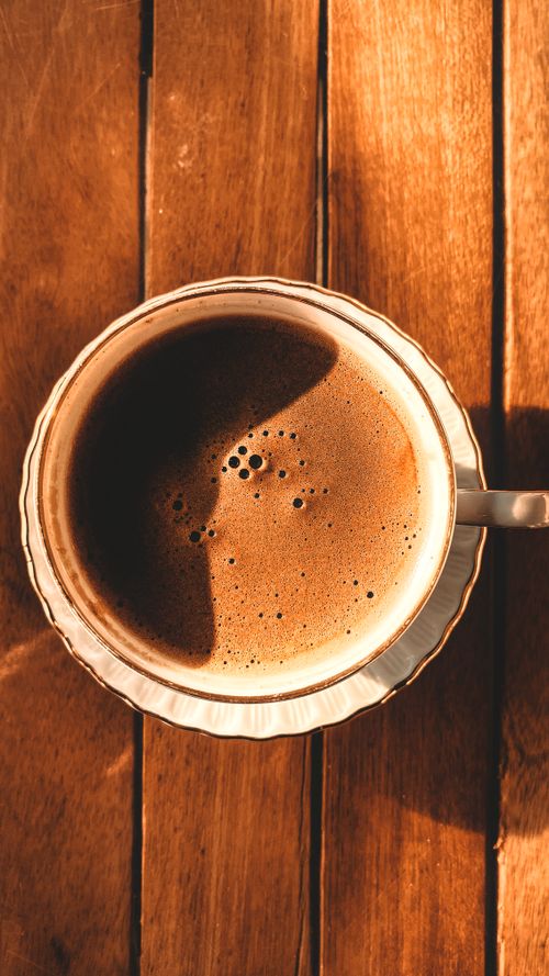 Free Top view of a cappuccino with frothy milk in a porcelain cup on a wooden surface, warm lighting. Stock Photo
