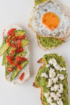 Flat lay of avocado toast variations with fried egg, feta, and tomatoes.