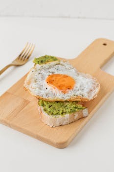 Appetizing avocado toast topped with a fried egg on a wooden board.